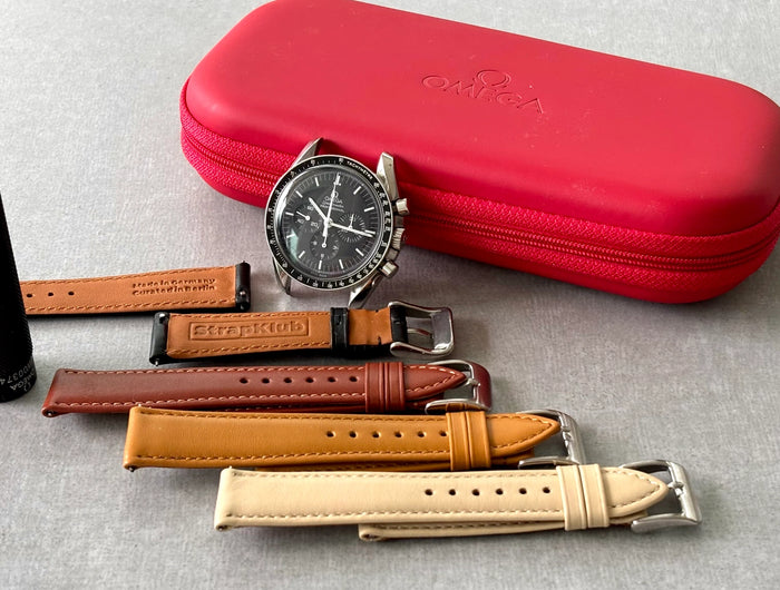 Omega Speedmaster, Wechselwerkzeug und Uhrenarmbänder vor rotem Omega-Etui